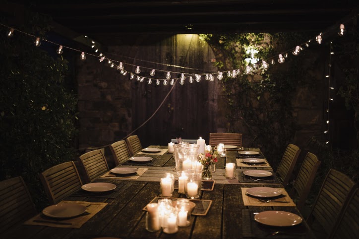 Night shot of a dressed garden table illuminated by candles and string lights.