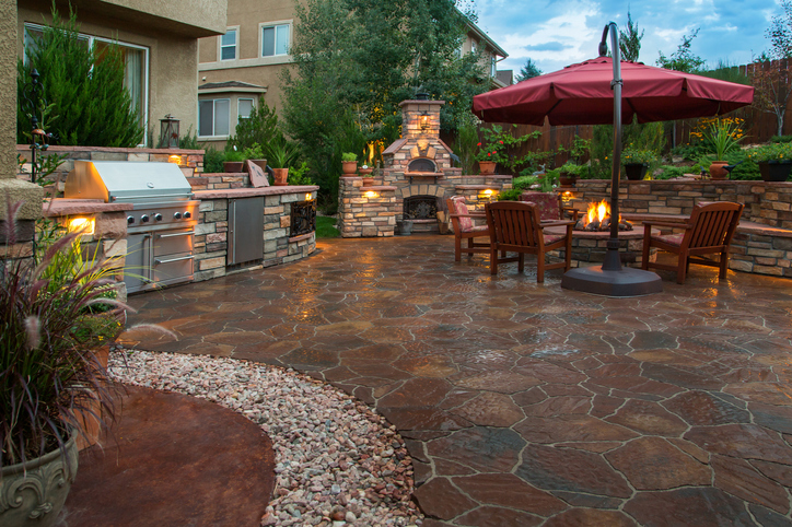 Paver patio with a fire pit, outdoor kitchen, pizza oven and lighting at dusk.