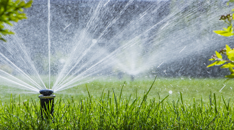 two irrigation sprinkler systems watering green grass in a lawn